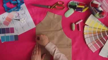 Bir terzinin iş yerinin üst görünümü ve bir giysi inşa etmek için gerekli aletler. Bir terzi pembe kumaşta sabunla bir desen çizer. Atıcı, tasarım ve terzilik kavramı.