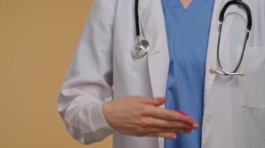 Tarafsız bej arka planda steteskoplu beyaz önlüklü doktor, farkındalığın sembolü olarak pembe kurdeleyle elini gösteriyor. Göğüs kanseri farkındalık günü, kadın sağlığı ve toplum kavramı.