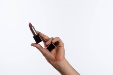 Gösterişli, siyah ve altın renkli bir çantasıyla lüks bir ruj tutan bir el şık makyaj için zengin pembe bir ton sunar..