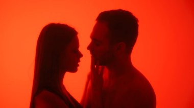 Kırmızı atmosferik ışıklandırmayla vurgulanmış, samimi ve romantik bir anı paylaşan bir çiftin silüeti..