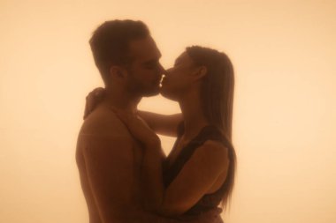 Siluetli bir çift, sıcak, çevresel aydınlatma, sevgi ve bağlantı ile yıkanmış samimi bir öpücüğü paylaşıyor..