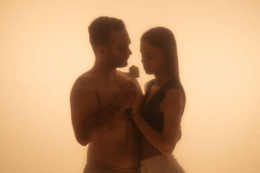 Hassas bir anı paylaşan bir çiftin silüetli aşk hikayesi aralarındaki yakınlığı ve sıcaklığı vurgular. Bir erkek bir kadına çiçek verir..