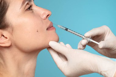 Dudaklara deri doldurucu enjeksiyonu için kullanılan bir şırınga ile yapılan kozmetik prosedürü gösteren yakın plan bir resim.