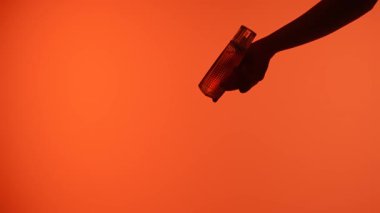 El silueti, turuncu bir arka planda parfüm şişesi takası yaparak çarpıcı bir görsel etki yaratıyor..