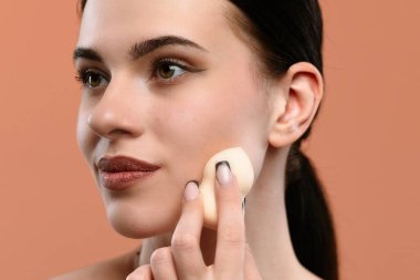 Bir kadın doğal güzelliğe sahip pürüzsüz bir ten elde etmek için makyaj süngeri kullanır..