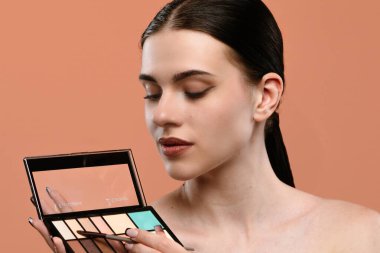 Bir kadın, parlak bir görünüş elde etmek için palet ve fırça kullanarak dikkatlice makyaj yapar..