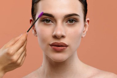 Bir makyaj sanatçısı görünüşünü geliştirmek için kaş jölesi sürer. Model doğal cilt tonlarıyla ileri bakar, hassasiyeti ve güzelliği vurgular..