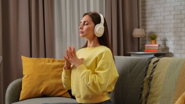 Kadın evde boş vakit geçiriyor. Genç bir kadın gününü evde, oturma odasındaki kanepede oturarak kulaklık takarak, akıllı telefon meditasyon podcastını dinleyerek ve nefes alma pratiği yaparak geçiriyor..