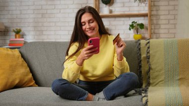 Kadın evde boş vakit geçiriyor. Genç bir kadın bütün gününü evinde, oturma odasındaki kanepede oturarak geçiriyor. Akıllı telefonunda kart numarası yazıyor. İnternetten alışveriş yapıyor..