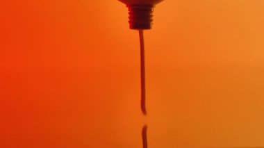 Kırmızı ve turuncu tonların pürüzsüz gradyan arkaplanında sıkıştırılan minimal yakın çekim bakım kremi.