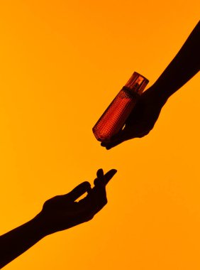 El silueti, turuncu bir arka planda parfüm şişesi takası yaparak çarpıcı bir görsel etki yaratıyor..