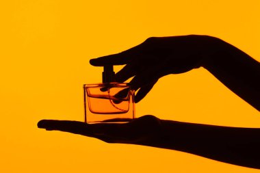 Zarif bir parfüm şişesinin silüeti parlak turuncu bir arka planda sergileniyor, parlak tasarımı ve modern estetiği vurgulanıyor..