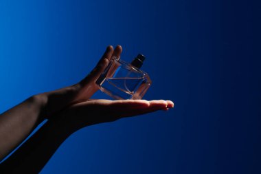 Zarif bir cam parfüm şişesi, zarif bir şekilde mavi bir arka fona karşı tutulmuş, sofistike ve stili temsil eden..