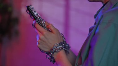 Bir kadının elleri cep telefonuyla metal bir zincir ile bağlanmış, teknolojik bağımlılığı sembolize ediyor..