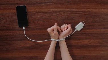 Telefon şarj kablosu ile bağlanan eller modern cihazlara ve teknolojik kısıtlamalara bağımlılığı simgeler.