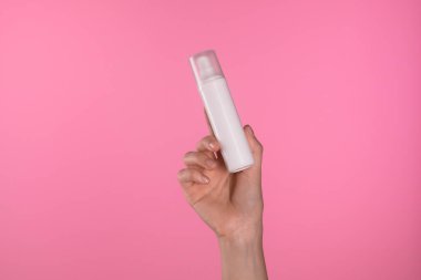 Beyaz bir kozmetik şişesi, pembe arka planda, minimalist güzellik ürünü tasarımı sergilenen bir el ile tutulur..