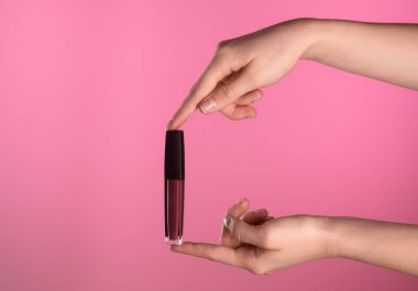 Canlı pembe bir arka plana karşı dudak parlatıcısını tutan bir elin yakın çekimi güzelliği ve tarzı gösteriyor..