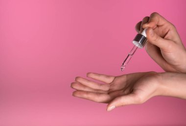 Bir damlatıcı, canlı pembe bir arka plana karşı serumun üzerine serumu bırakıyor, cilt bakımı uygulamasını gösteriyor.