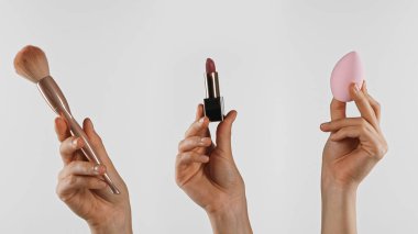 Makyaj fırçası, ruj ve güzellik blenderi tutan bir el. Kusursuz bir makyaj uygulaması için gerekli araçlar.