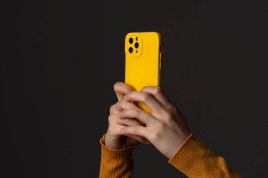 Koyu bir arkaplan karşısında sarı çantalı akıllı telefon tutan birinin yakın plan fotoğrafı..