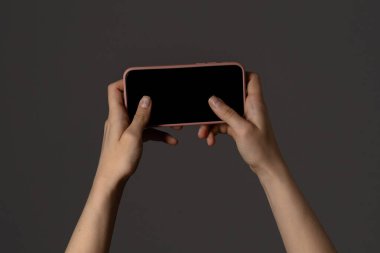 Eller bir akıllı telefonu yatay olarak siyah bir ekranla karanlık bir arkaplan üzerinde tutar, dijital bir cihazın odak noktasını yakalar.