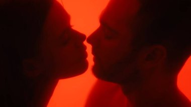 Romantik bir çift silueti samimi bir anda, sıcak kırmızı bir parıltıyla vurgulanır, tutkuyu yansıtır..