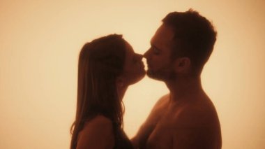 Siluetli bir çift, sıcak, çevresel aydınlatma, sevgi ve bağlantı ile yıkanmış samimi bir öpücüğü paylaşıyor..