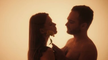 Bir erkek, bir kadının yüzüne çiçekle dokunur. Hassas bir anı paylaşan bir çiftin siluet aşk hikayesi aralarındaki yakınlığı ve sıcaklığı vurgular..