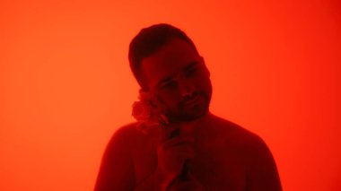 Bir adam bir çiçeği portakal arkaplanına dayayıp sakin ve düşünceli bir atmosfer yaratıyor..