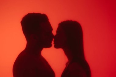Kırmızı cam bir yüzey arkasında öpüşen bir çiftin tutkulu silueti samimiyet ve gizemi vurguluyor..