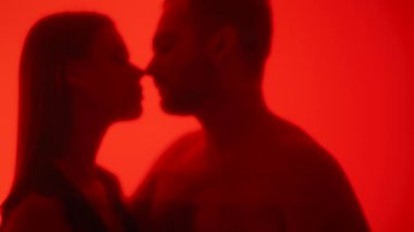 Kırmızı cam bir yüzey arkasında öpüşen bir çiftin tutkulu silueti samimiyet ve gizemi vurguluyor..