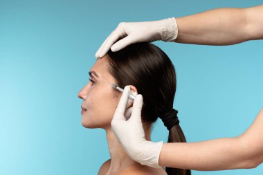 Estetik ameliyat sırasında yüz enjeksiyonu yaptıran bir kadının yakın çekimi. Görüntü, kozmetik tedavilerdeki hassasiyet ve özeni vurguluyor.