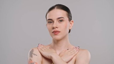 Bir kadın stüdyo resminde zarif bir poz veriyor, kolunda çapraz ellerle narin bir dövme gösteriyor..