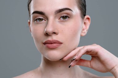 Doğal güzelliği olan bir kadını gösteren yakın plan bir portre. Makyajı az, cildi pürüzsüz. Yüz hatları belirgin..