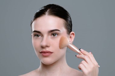 Makyaj fırçası kullanan bir kadın yanağına makyaj malzemesi sürerek cilalı bir görünüm elde ediyor..