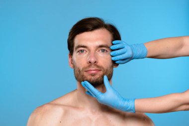 Mavi eldiven giyen bir kozmetolog estetik geliştirme prosedürleri için erkek hastaları muayene ediyor. Klinik ortamdaki erkekler için cilt bakımı ve güzellik danışmanlığı.