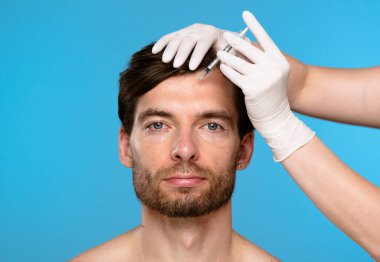 Bir kozmetolojistin elleri bir adama şırınga enjekte ediyor. Güzellik, gençleşme ve cildin nemlendirilmesi, yüzündeki kozmetik kusurların giderilmesi..