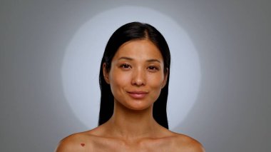 Doğal bir ifade, pürüzsüz bir ten ve omzunda ince bir dövme olan bir kadını gösteren bir portre. Arkaplan tarafsız, konuya odaklanmış durumda..