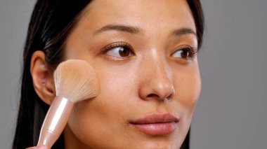 Makyaj fırçasının yakın çekimi bir kadının yanağına pudra sürerken pürüzsüz bir cilt ve hassasiyet vurguluyor..