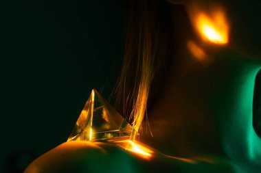 Omzunda şeffaf prizma olan bir kadının sanatsal çekimi. Renkli ışık yansımaları fütürist ve gizemli bir görsel atmosfer yaratır..