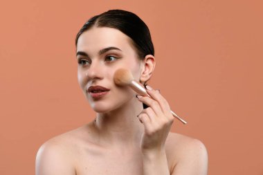 Bir kadın yumuşak bir fırça kullanarak makyaj yapıyor, kusursuz ve doğal bir cilt görünümü elde etmeye odaklanıyor..