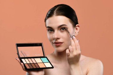 Bir kadın, bir paletten makyaj yapmak için göz farı kullanıyor. İnce, zarif uygulama teknikleri gösteriyor..