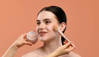 Bir kadın makyajını toz fırçasıyla yapar, doğal ve kusursuz bir görünüme odaklanır..