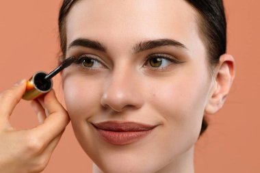 Bir kadının kirpiklerine rimel sürerken, güzellik ve makyaj tekniklerini vurgularken..