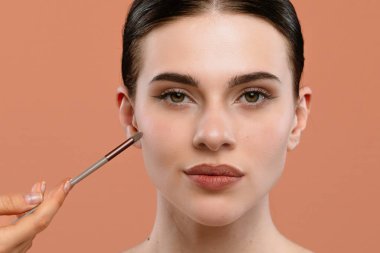 Doğal bir ifadeyle yanaklarını fırçalayıp yumuşak bir arka plana makyaj yapan bir kadın..