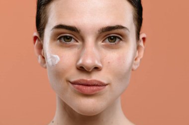 Yanağına doğal makyaj ve cilt kremi sürmüş bir kadının portresi cilt bakımını ön plana çıkarıyor..