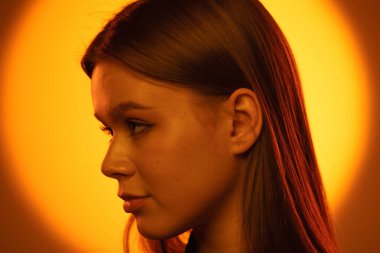 Bir kadın profili turuncu renkli ışıktan zarifçe ortaya çıkar, sükuneti ve tefekküre vurgu yapar..