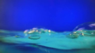 Turkuaz su yüzeyinde yüzen hava kabarcıklarıyla hafif dalga hareketi. Canlı bir mavi arkaplan karşısında minimalist sualtı kompozisyonu.