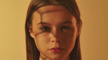 Yüzünde geometrik gölgeler olan genç bir kadının yumuşak turuncu arka planına yakın çekim. Güzellik, cilt bakımı ve duygusal fotoğrafçılık konuları için mükemmel..