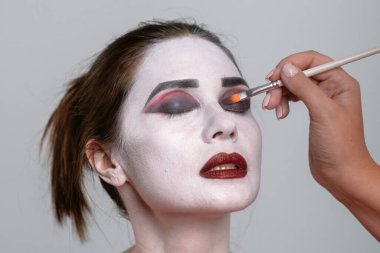 Kalın renklerle sanatsal makyaj yaptıran birinin yakın çekimi. Başvuru sürecine odaklanıldı.